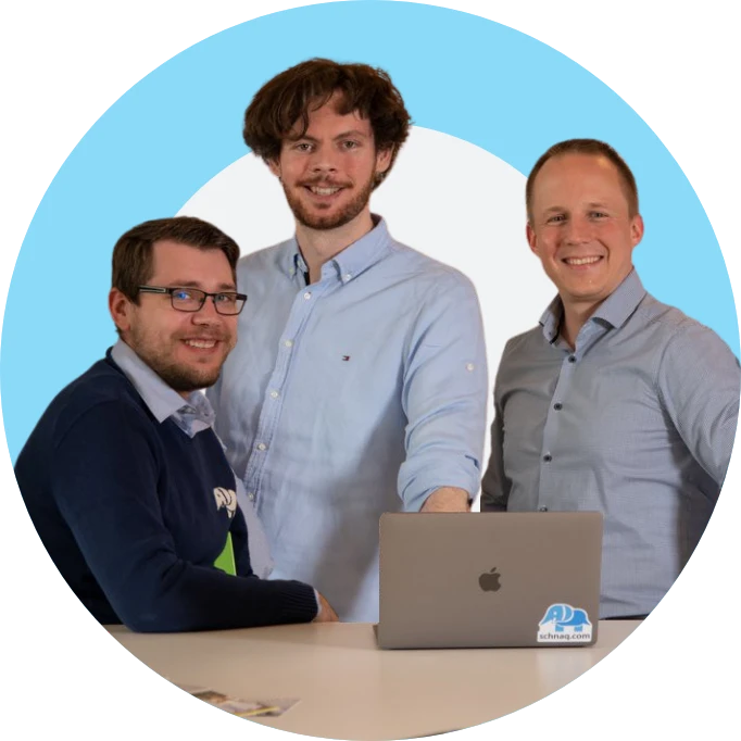 Ein Bild von den Gründern von schnaq Consulting / schnaq GmbH. Alle drei schauen in die Kamera und lächeln. Im Vordergrund ist ein Laptop auf einem Tisch zu sehen.